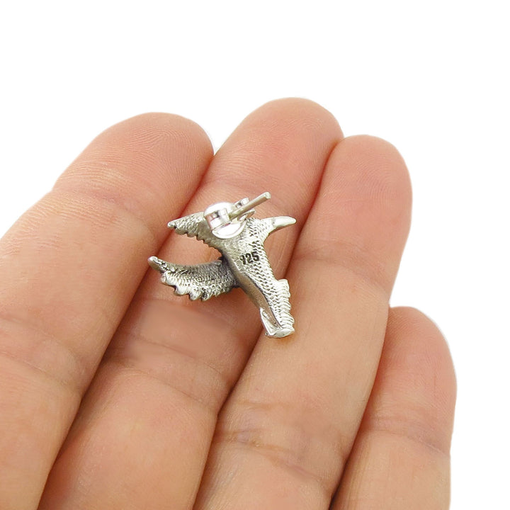 Reverse of a 925 sterling silver stud earring in the shape of a bird held between fingers on a white background