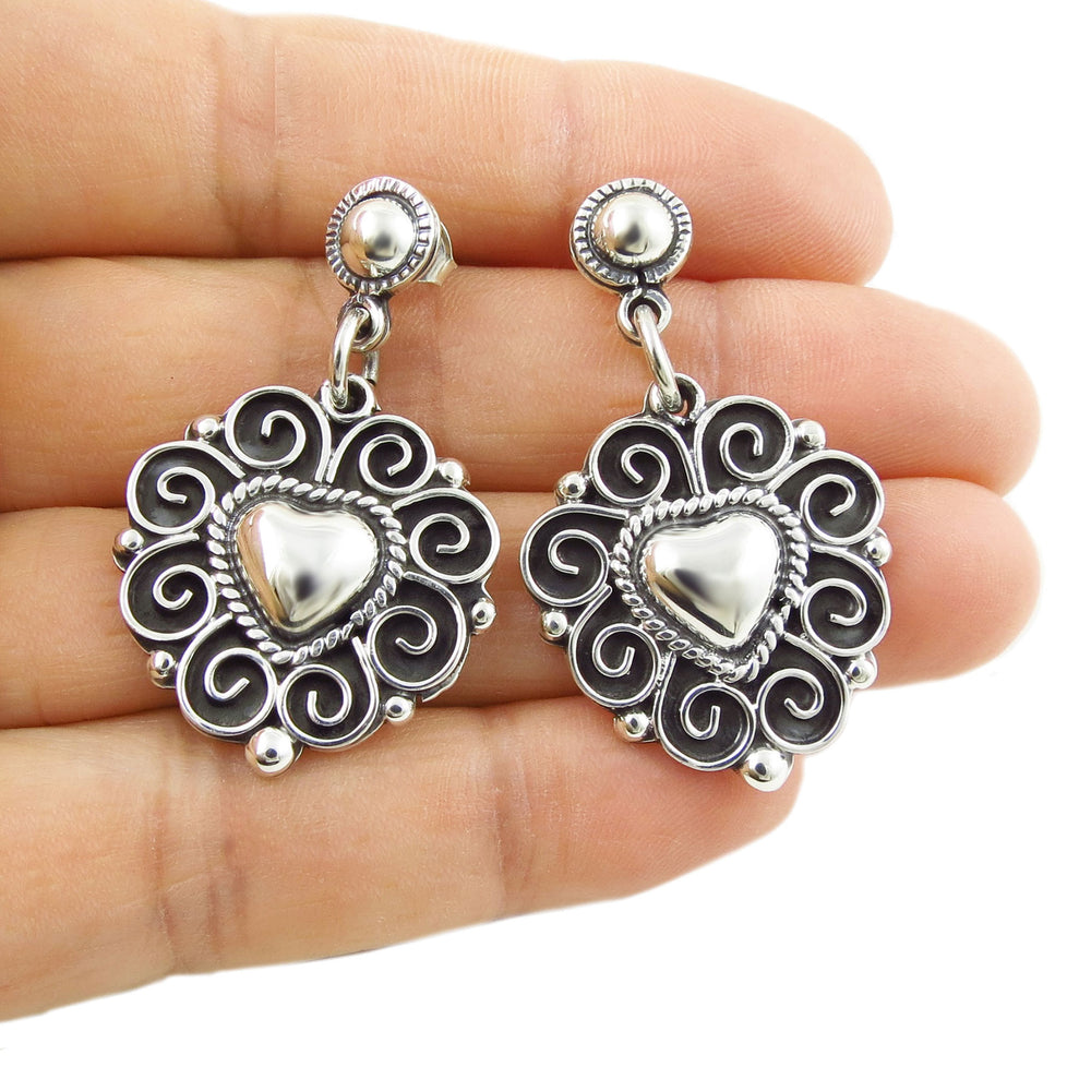 Mexican 925 sterling ilver heart-shaped earrings held between fingers on a white background