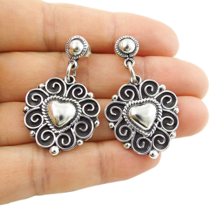 Mexican 925 sterling ilver heart-shaped earrings held between fingers on a white background