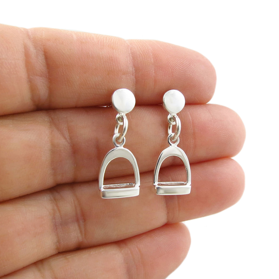 Sterling 925 Silver equestrian-themed horse stirrup dnagle earrings held between fingers on a white background