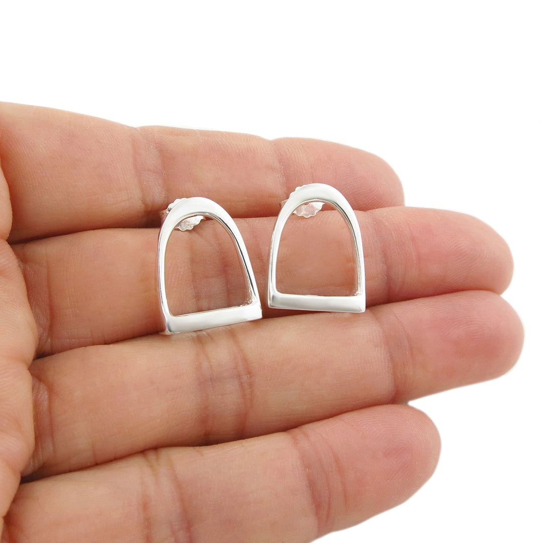 Large 925 sterling silver equestrian horse  stirrup earrings held between fingers on a white background