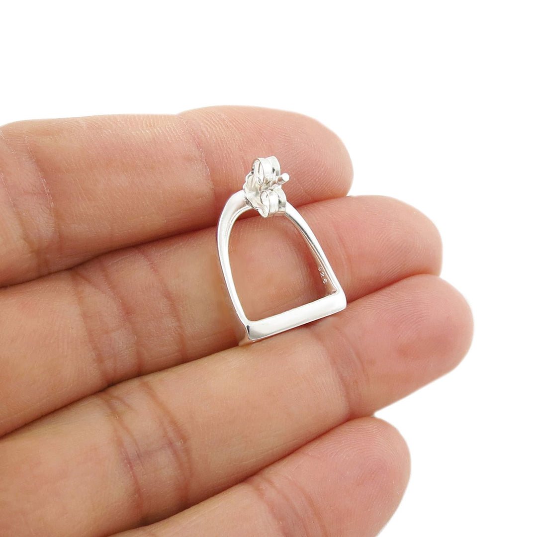 A large 925 sterling silver horse stirrup earring showing the post fastener held between fingers on a white background
