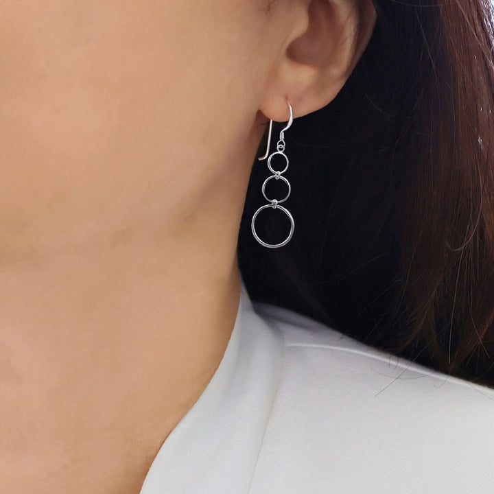 Long 925 sterling silver triple infinity circle dangle earrings worn by a woman with dark hair.