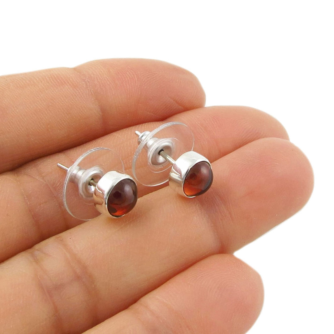 Silver stud earrings with red garnet gemstones held between fingers on a white background