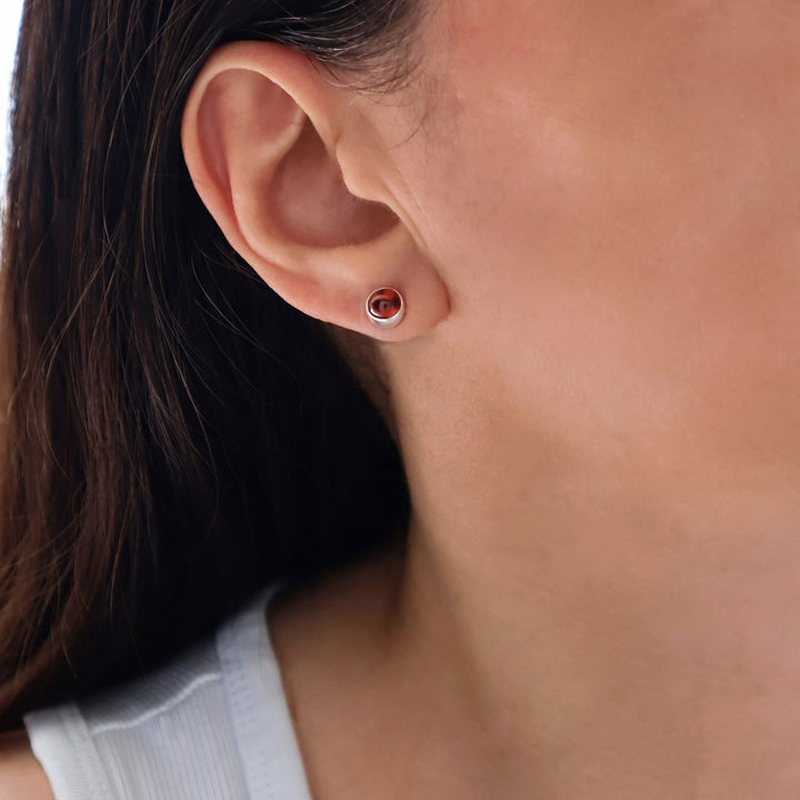 Close-up of an woman's ear wearing a small round 925 earring silver stud earring with a red garnet natural stone. 