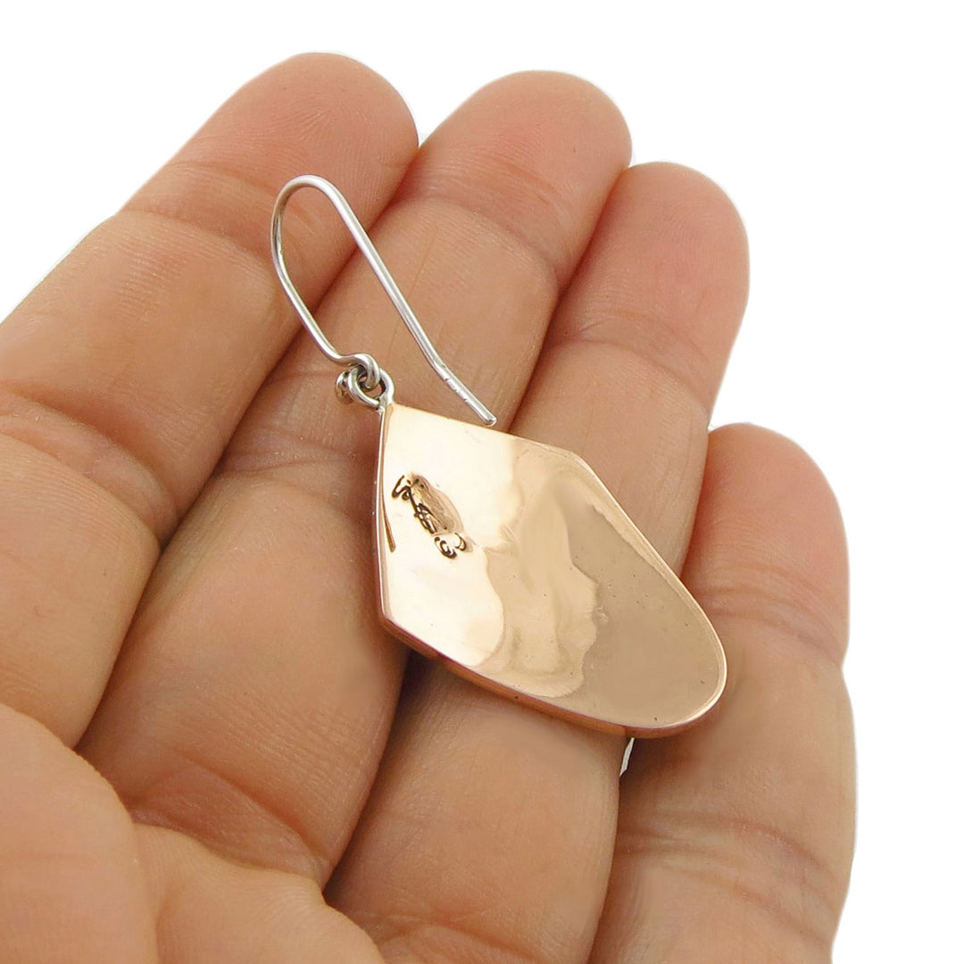 Large copper and 925 silver teardrop-shaped earring held between a woman's fingers on a white background