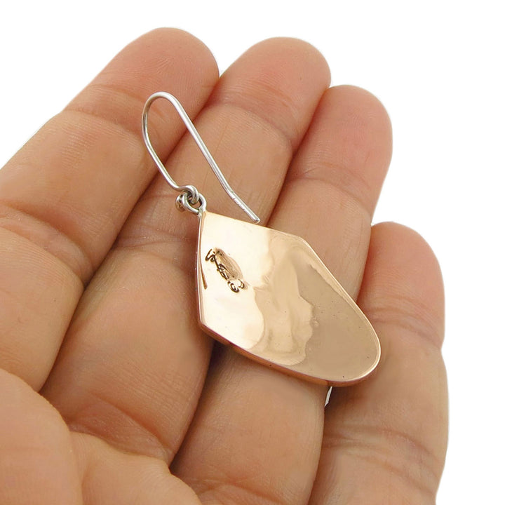 Large copper and 925 silver teardrop-shaped earring held between a woman's fingers on a white background