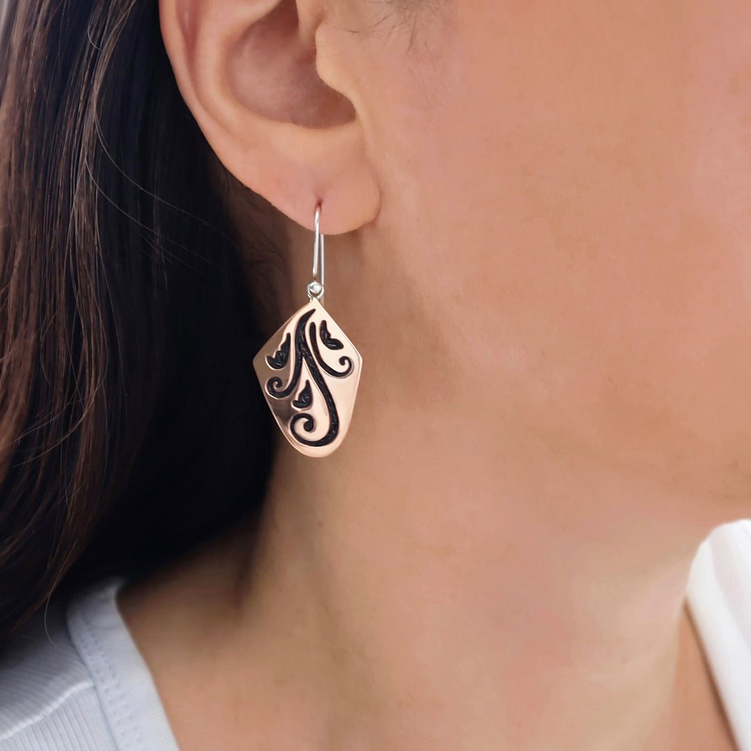 Close-up of a woman wearing a decorative two tone copper and 925 silver earring with intricate design.