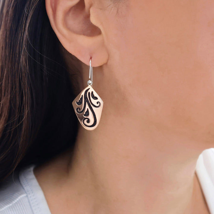 Close-up of a woman wearing a decorative two tone copper and 925 silver earring with intricate design.
