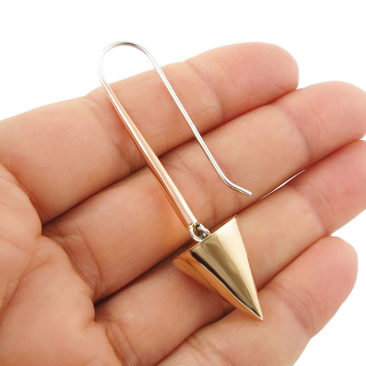 A single two tone 925 silver and copper spike threader hook earring held in a woman's hand against a white background