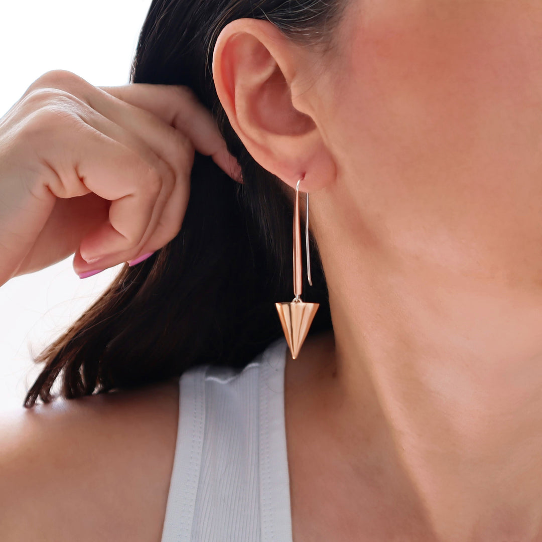 Long mixed metal copper and 925 silver spike drop earrings being worn by a woman with a blurred background