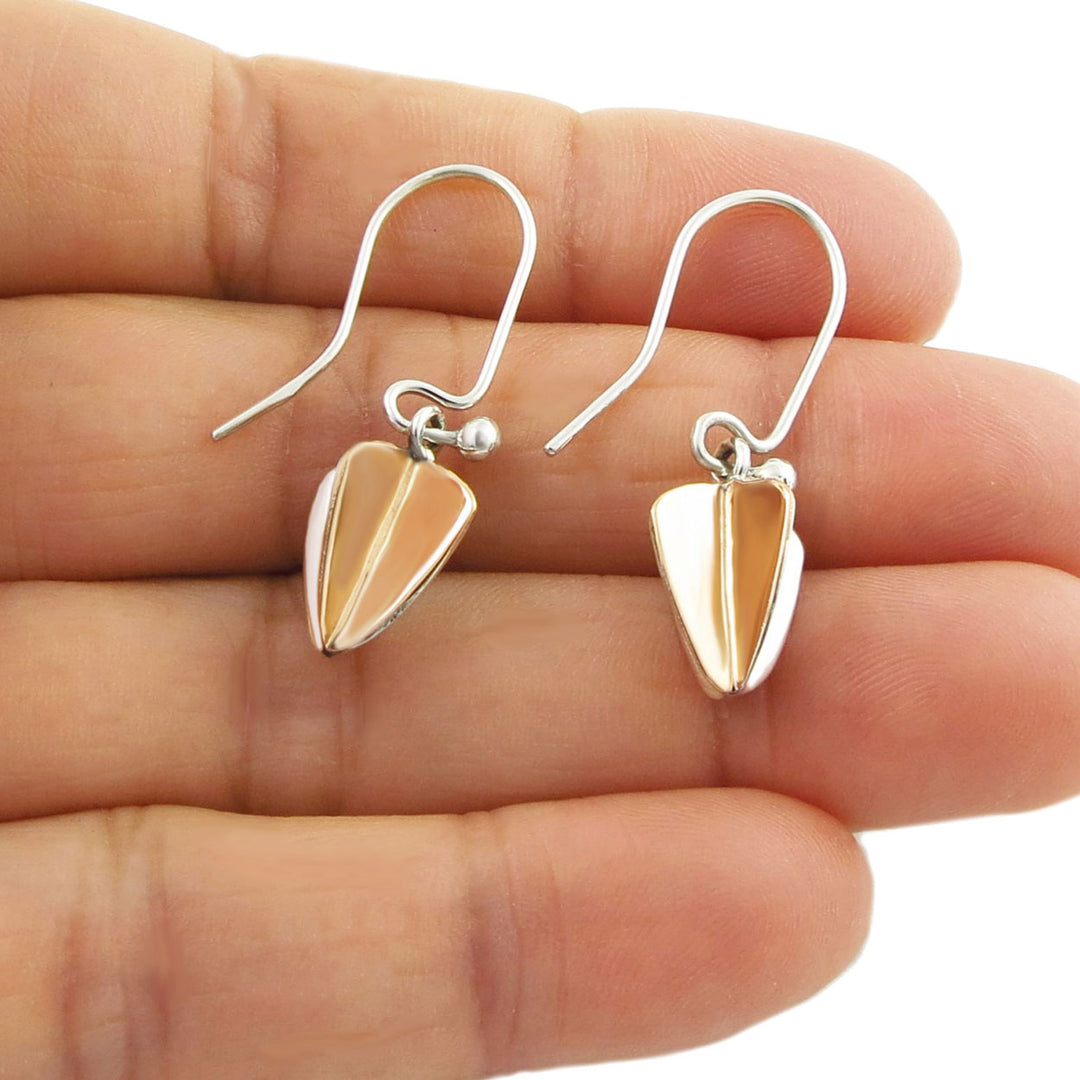 Pair of two tone copper and silver earrings held between fingers on a white background