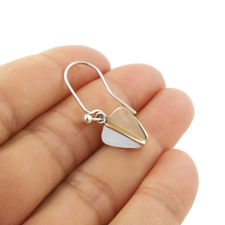 Mixed metal copper and sterling 925 silver earring with sculpted dangling drops held between a woman's fingers on a white background