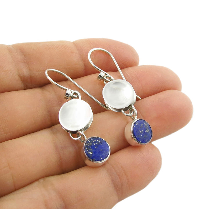 Dangling 25 silver drop earrings with blue lapis lazuli gemstones held in a woman's hand against a white background