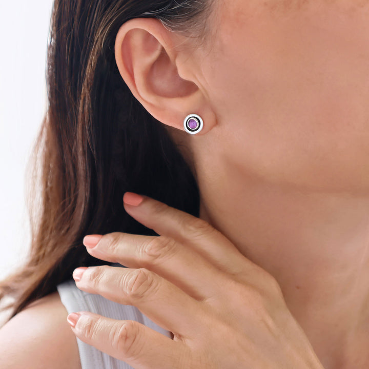 Close-up of a woman wearing a sterling 925 silver round stud earring with a amethyst gemstone and a hand adjusting it.