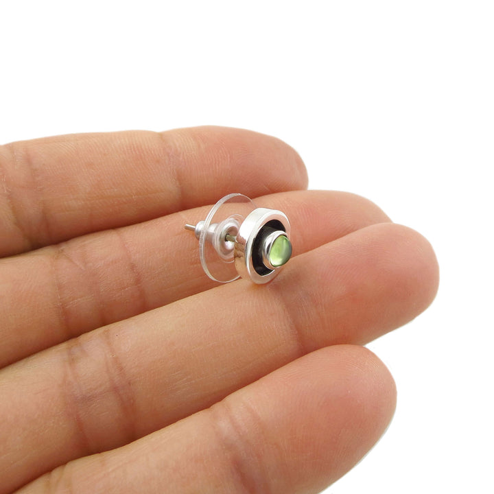 Small sterling 925 silver stud earring with a green peridot gemstone held between fingers on a white background