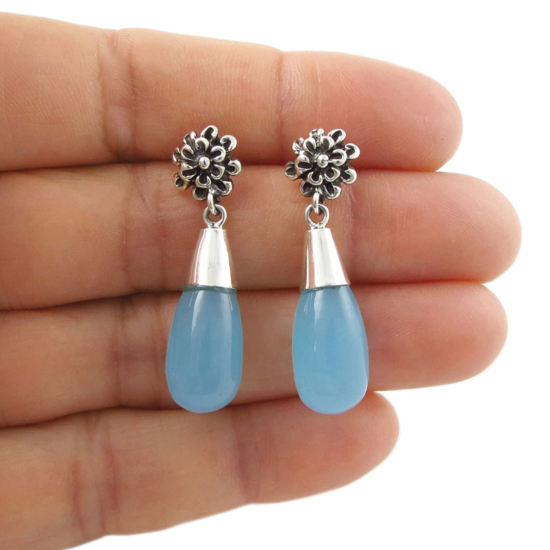 Pair of 925 sterling silver and blue chacedony gemstone teardrop earrings held between fingers on a white background