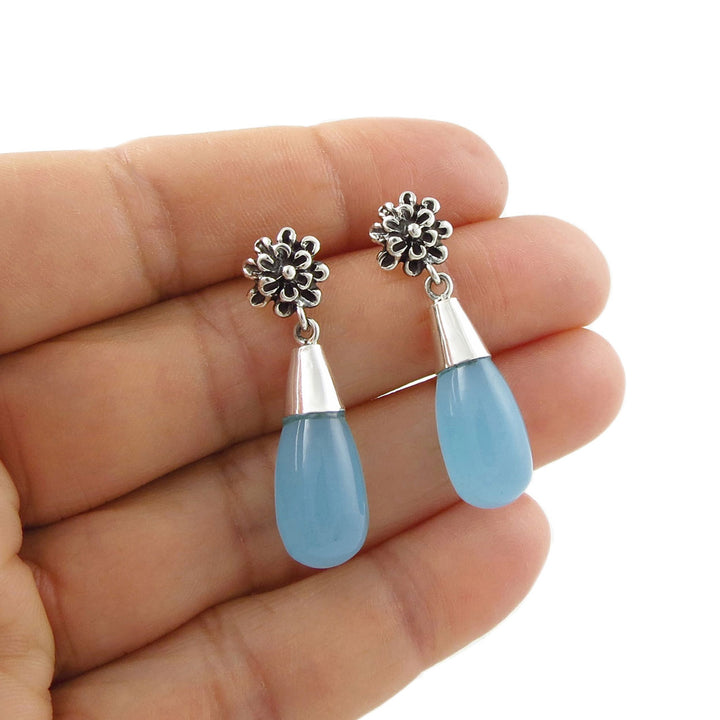 Blue chalcedony gemstone teardrop earrings with 925 silver floral tops held in a hand against a white background