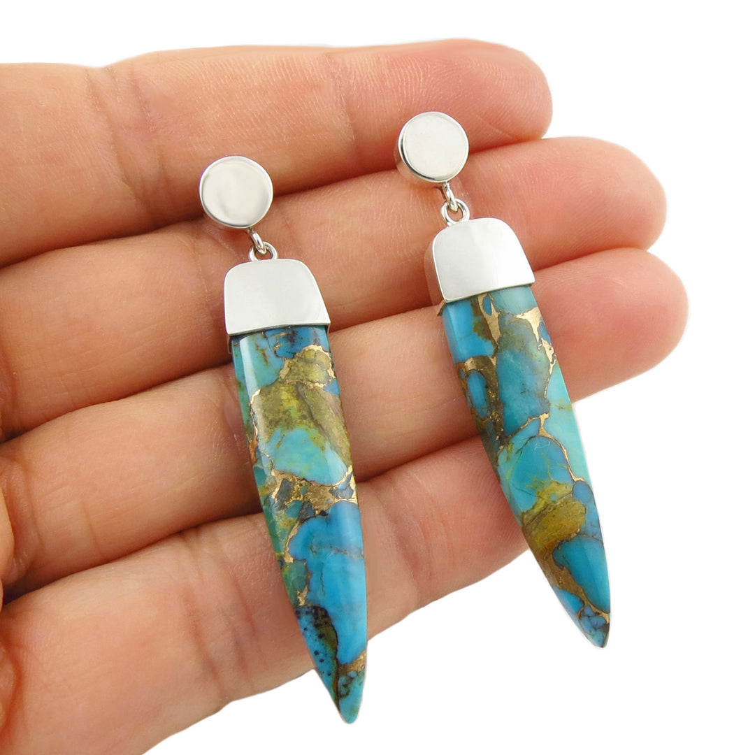 Turquoise gemstone earrings with sterling 925 silver accents held in a woman's hand against a white background