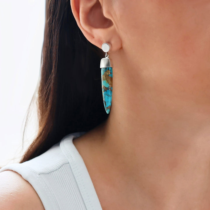 Long turquoise gemstone 925 silver earrings worn by a woman with a neutral background