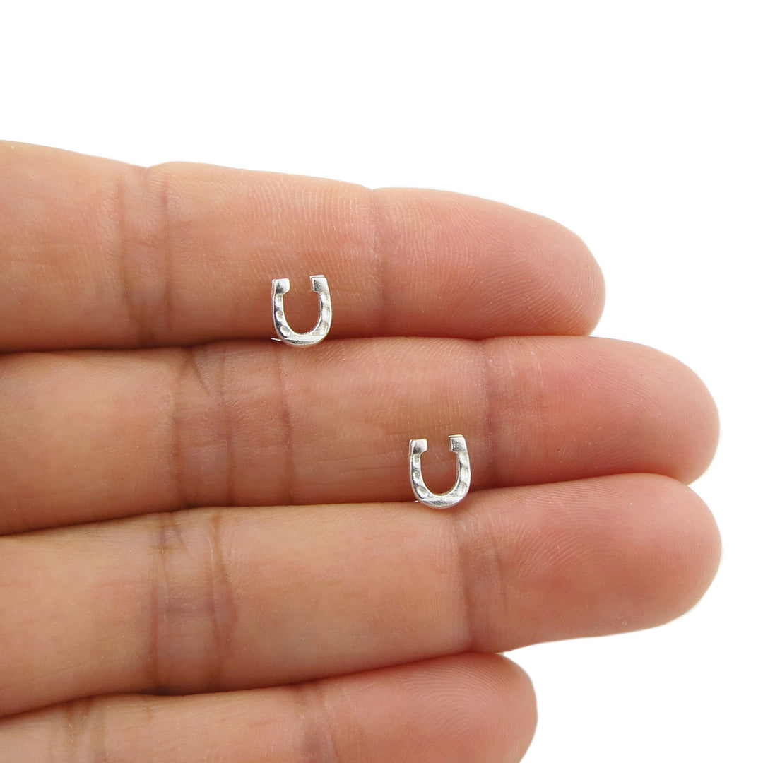 Two small 925 silver horseshoe stud earrings for women displayed on a person's fingers against a plain white background.