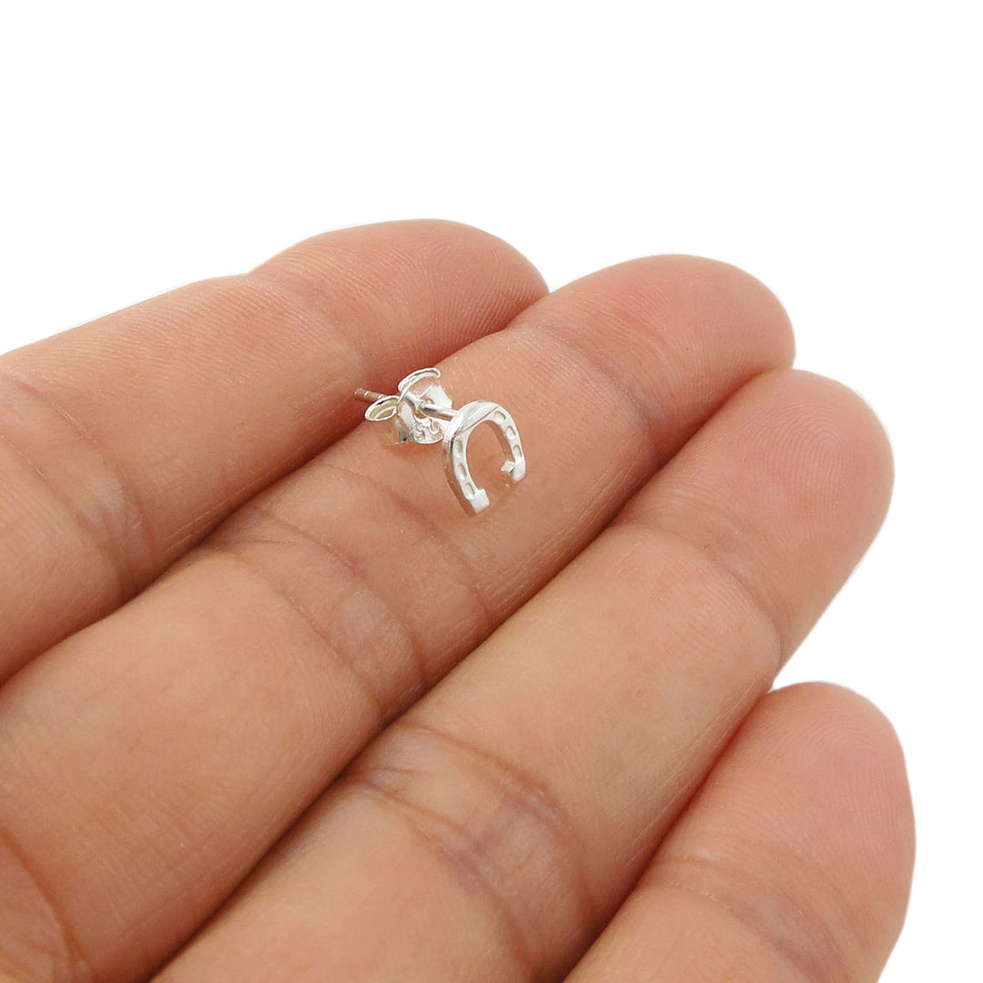 A tiny 925 sterling silver ladies earring shaped like a stylised horse shoe shown resting on a person's fingers against a plain white background.