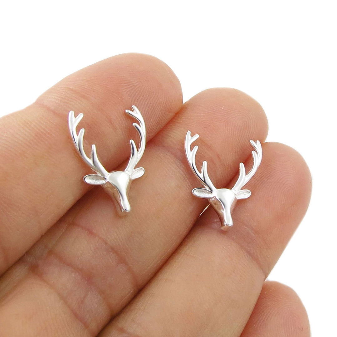 A pair of large 925 silver reindeer stag head stud earrings resting on a person's fingers against a plain white background.