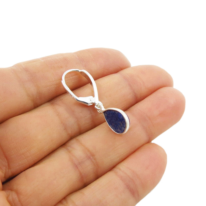 Teardrop-shaped blue lapis lazuli gemstone earring with a lever ack hook held between a woman's fingers against a white background