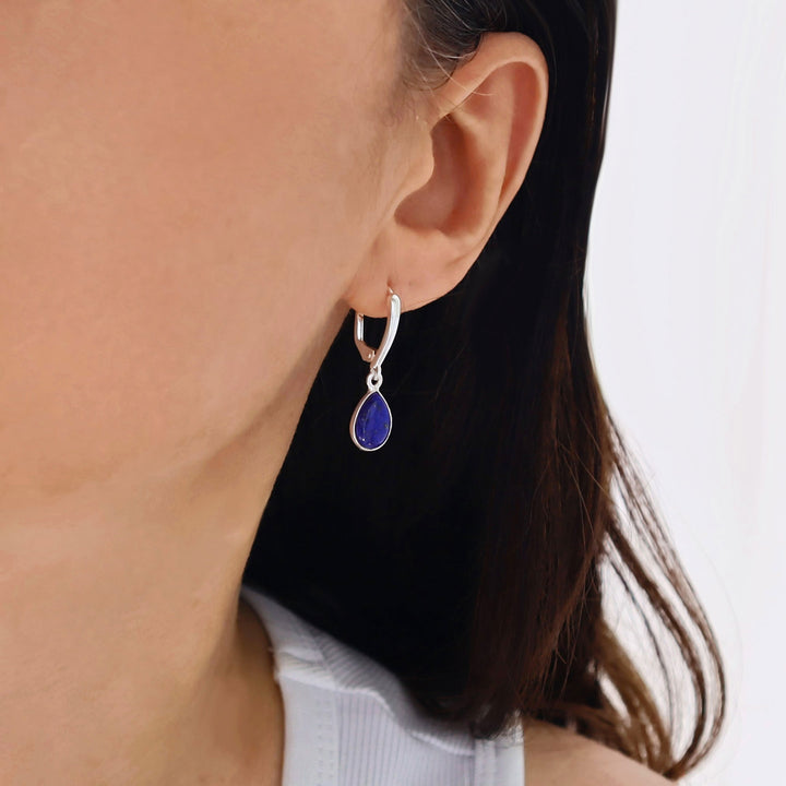Close-up of a woman wearing a sterling 925 silver earring with a lever back hook and a blue lapis lazuli dangling teardrop gemstone. 
