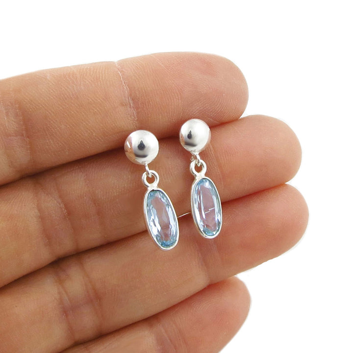 Sterling 925 Silver earrings with faceted blue topaz gemstones held between fingers on a white background