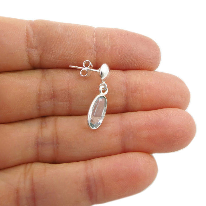 Sterling 925 Silver earring with a faceted blue topaz  gemstone held between fingers on a white background