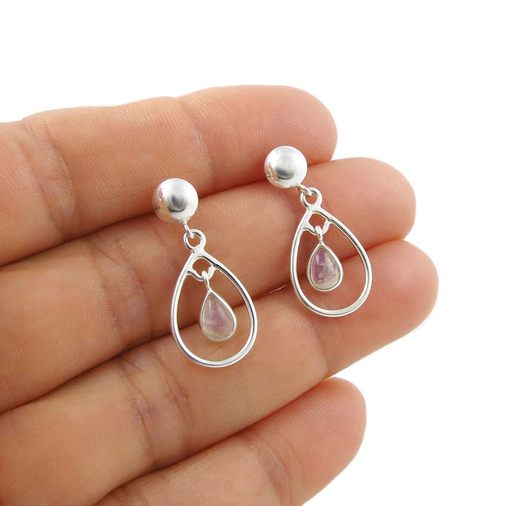 A pair of 925 sterling silver teardrop dangle earrings with pear-shaped pinkish-purple rainbow moonstones, shown resting on a woman's fingers against a white background.