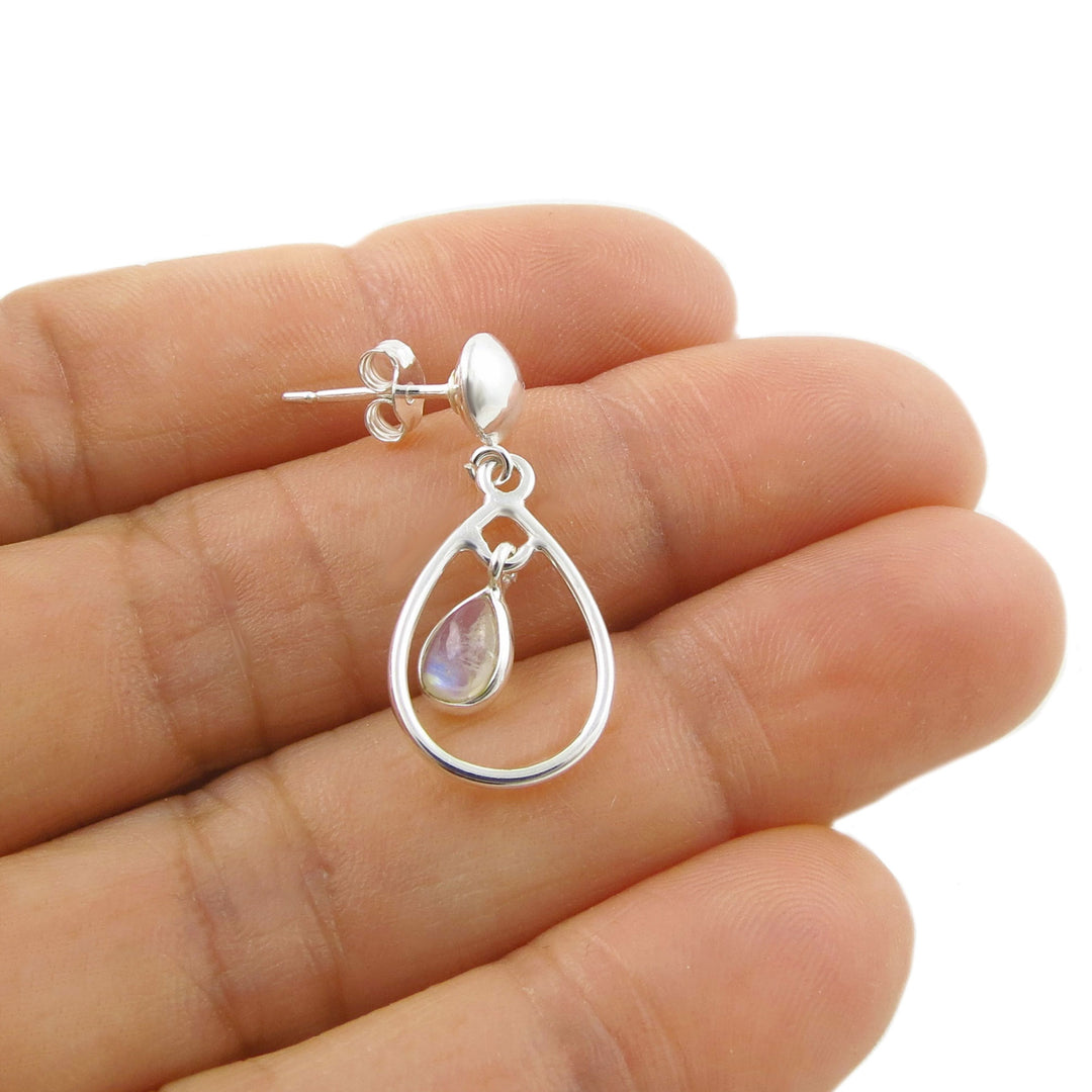 A sterling 925 silver teardrop dangle earring with a small iridescent teardrop rainbow moonstone gemstone, shown resting on a person's fingers against a white background.