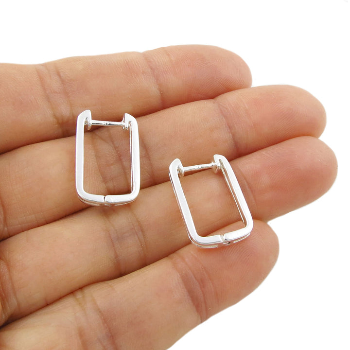 A pair of polished 925 silver rectangular hoop earrings resting on a woman's palm against a white background.
