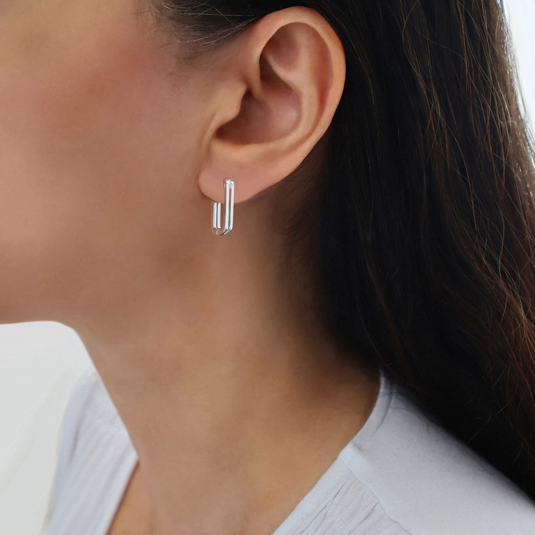 A close-up of a model's ear wearing a pair of polished 925 silver huggie hoop earrings with a double-bar design.