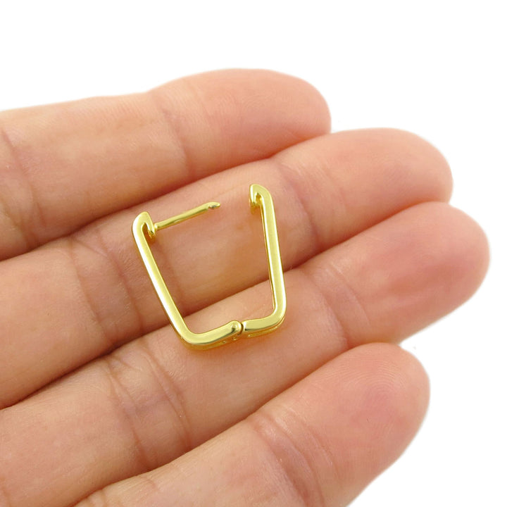 A mid sized rectangle 9ct gold ear cuff or hoop open single earring resting on a person's palm, shown against a plain white background.