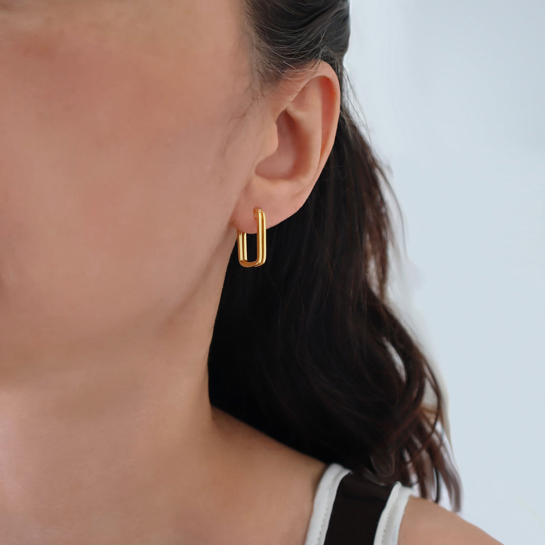 A close-up of a model's ear wearing a mid sized 9ct gold plated huggie hoop earring.