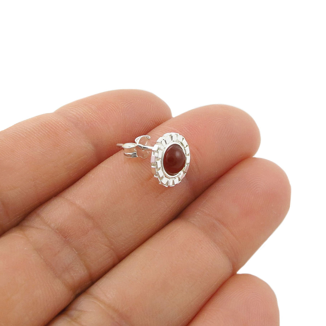A sterling 925 silver stud earring with an round reddish-brown carnelian cabochon gemstone, shown resting on a person's fingers against a plain white background.