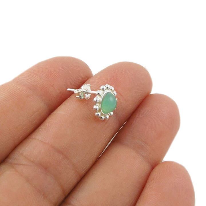 A close-up of a hand holding a small 925 silver stud earring with an round light green chrysoprase stone and a halo of small clear stones, shown against a plain white background.