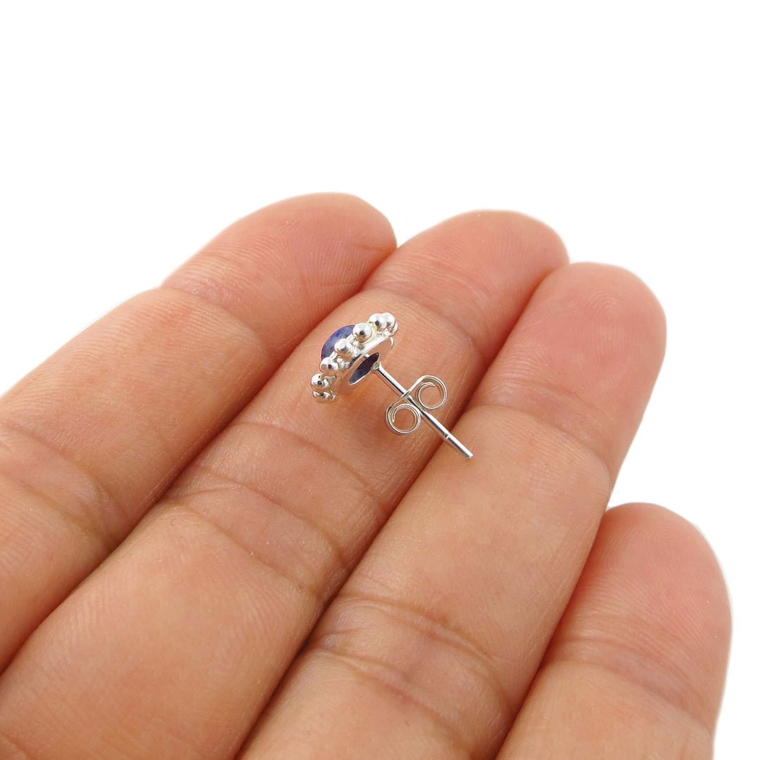 A 925 silver stud earring with a small round blue lapis lazuli gemstone, shown resting on a person's fingers against a white background.