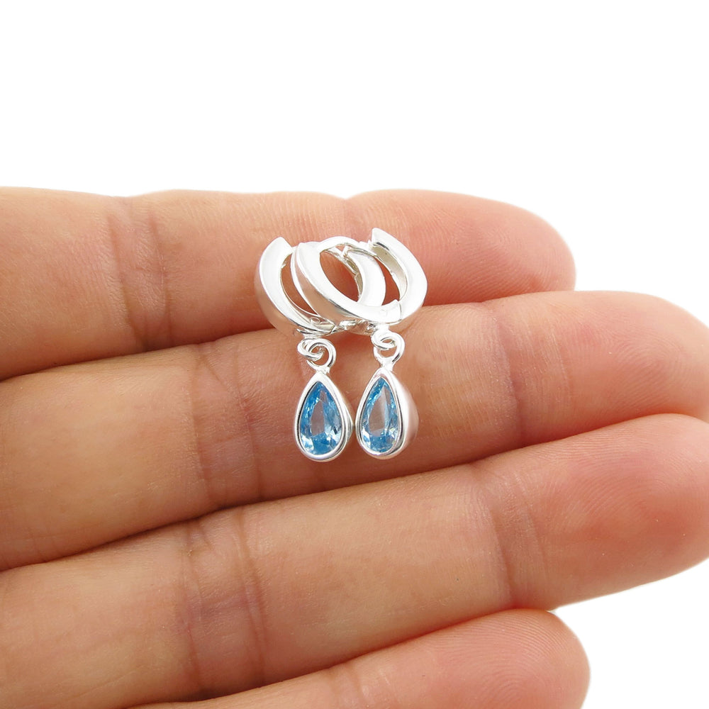 A pair of 925 sterling silver hoop earrings with dangling teardrop-shaped light blue aquamarine gemstones, shown resting on a person's hand against a white background.