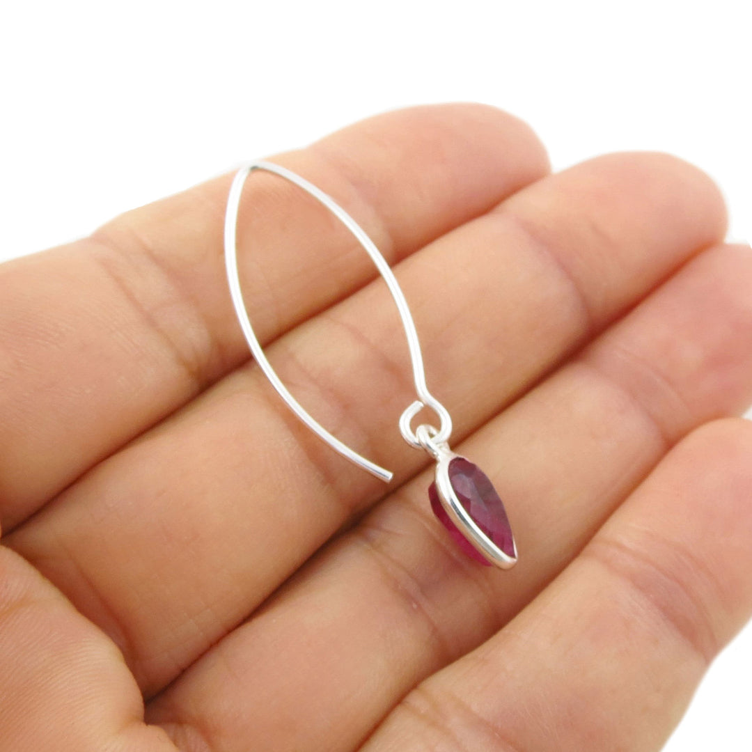 A silver crescent-shaped hoop earring with a small teardrop-shaped pink ruby quartz gemstone pendant, shown resting on a person's hand against a white background.