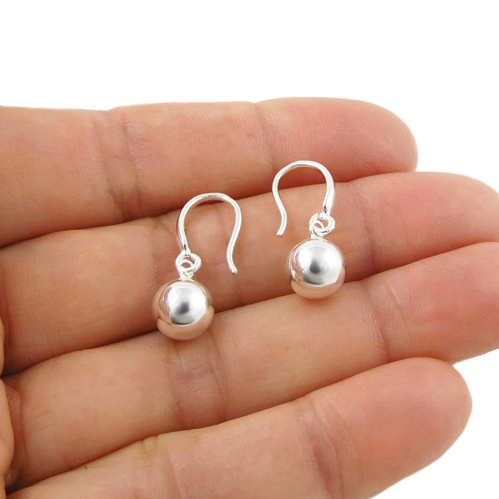 A pair of silver dangle earrings with polished round ball beads and fish hook backs, shown resting on an open hand for scale against a white background.