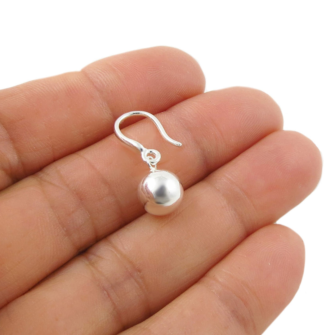 A single sterling 925 silver dangle earring with a polished spherical bead and fish hook ear wire, shown resting on a person's palm against a white background.