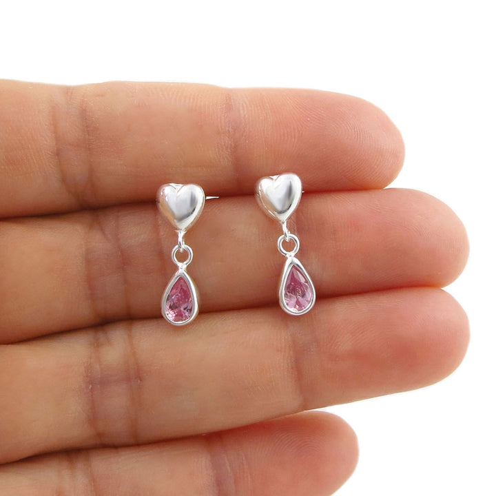 A pair of 925 silver heart and teardrop dangle earrings with pink tourmaline crystals, shown resting on a person's hand against a white background.