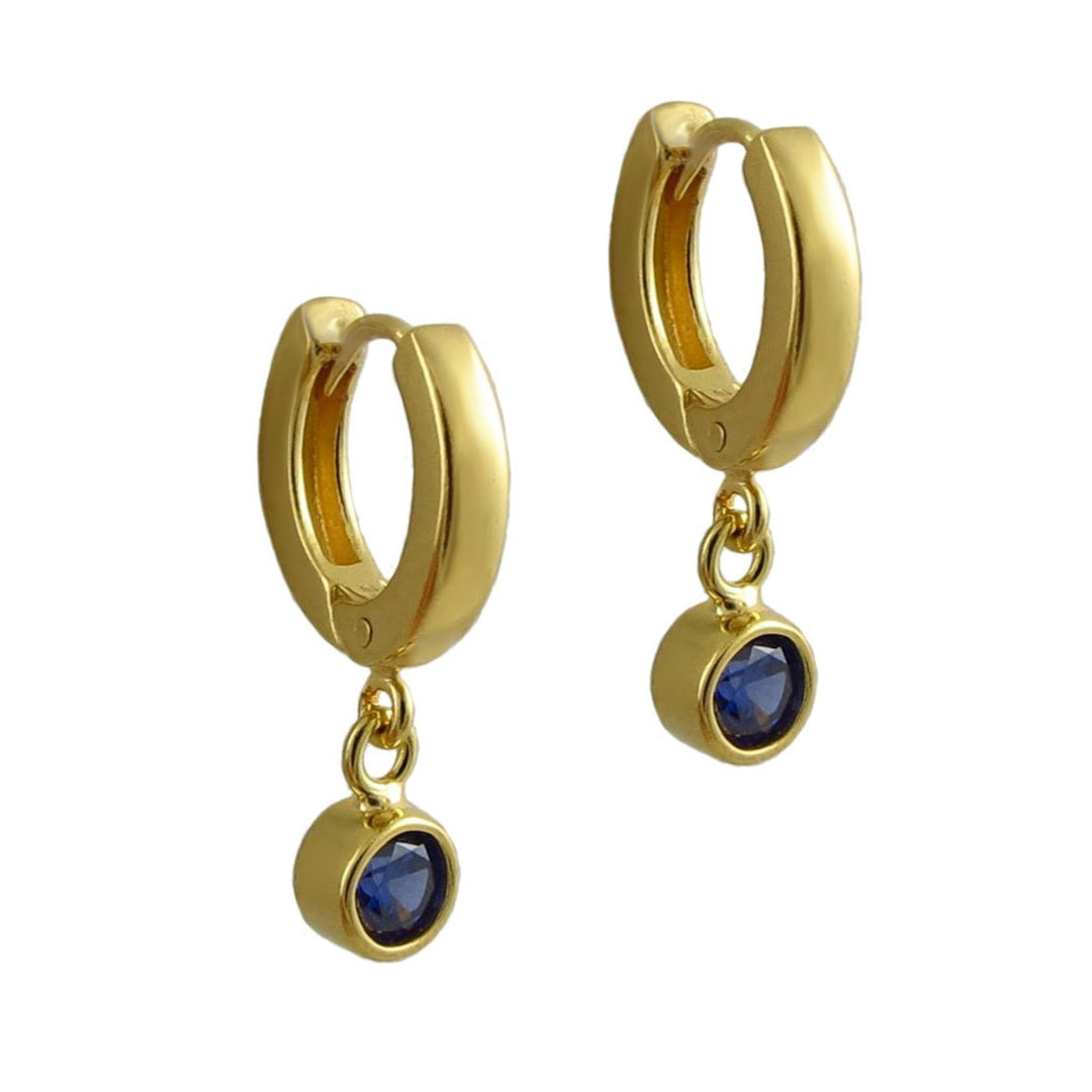 A pair of gold huggie hoop earrings with a dangling round blue sapphire gemstone, shown on a plain white background.