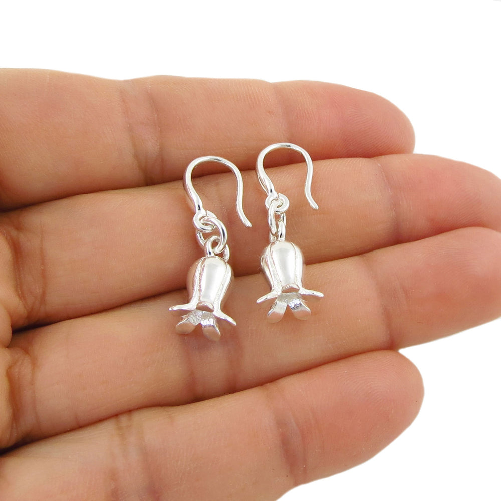 A pair of silver dangling earrings shaped like small blluebell flowers, shown resting on an open hand against a white background.