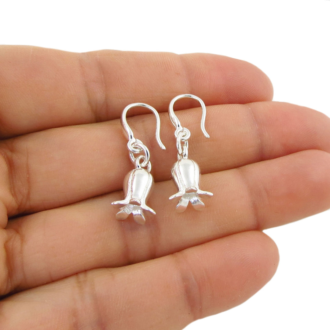 A pair of silver dangling earrings shaped like small blluebell flowers, shown resting on an open hand against a white background.