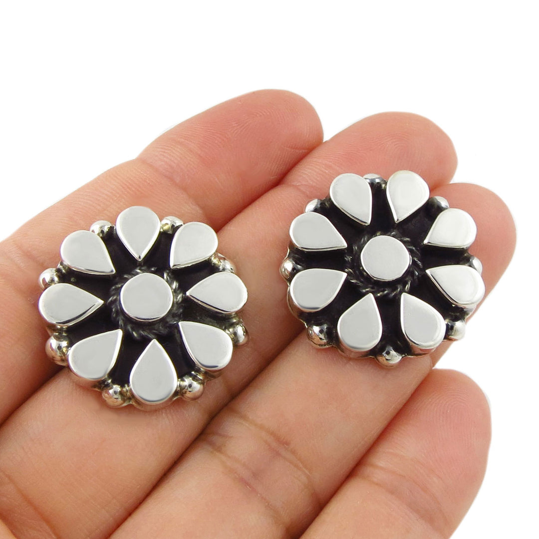 A pair of large sterling 925 silver daisy flower  earrings displayed on a person's fingers against a plain white background.