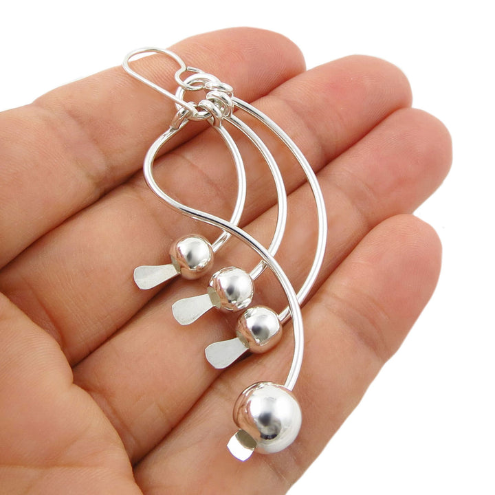 A pair of sterling 925 silver drop earrings with dangling bead charms, held in a person's hand against a white background.